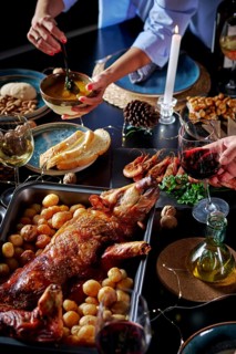 Cropped unrecognizable woman's hands serving sauce next to a table set with a roasted suckling pig,
