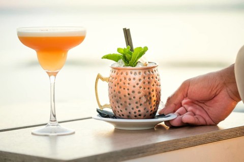 A beautifully crafted cocktail and a refreshing Moscow Mule are served on a beachside table at
