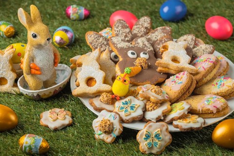Decorated Easter cookies on a plate with a ceramic rabbit figurine and colorful eggs in the grass