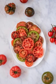 A variety of colorful heirloom tomatoes, sliced and arranged on a white plate, showcasing their