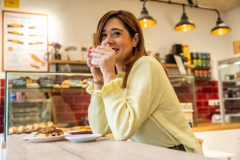 Woman smiling at a cozy cafe counter, holding a warm coffee mug and relaxing while enjoying a