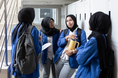 Group of Asian Muslim student wearing hijabs and school uniforms gather around lockers, engaging in