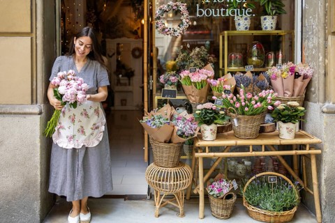 A cheerful woman stands at the entrance of her charming flower shop, holding a bouquet of fresh