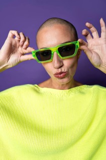 A middle-aged woman with a shaved head poses confidently against a purple background, wearing