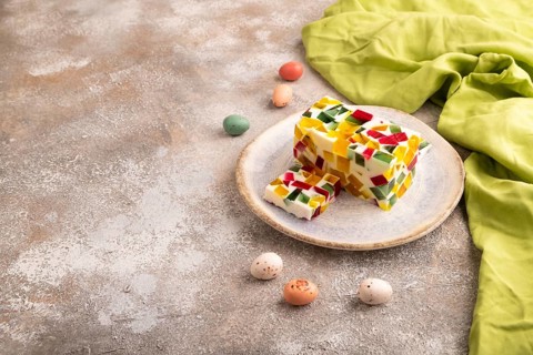 Colored Fruit and milk jelly on brown concrete background and green linen textile, side view, copy
