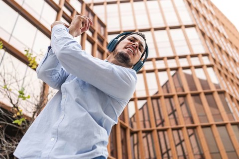A Cuban man in headphones dances energetically, filled with rhythm, against an urban backdrop. His
