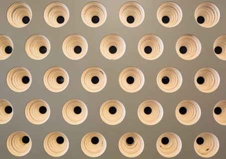 An intricate geometric pattern of evenly spaced round wooden structures with black centers on a