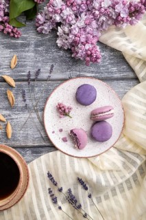 Purple macarons or macaroons cakes with cup of coffee on a gray wooden background and white linen