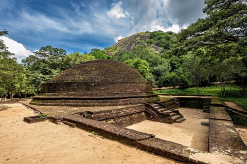 Round stupa on an open area with blue sky and green surroundings, temple ruins near Sigiriya in Sri