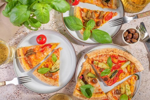 A rustic scene featuring vegetarian pizza slices topped with fresh basil, zucchini, eggplant, and