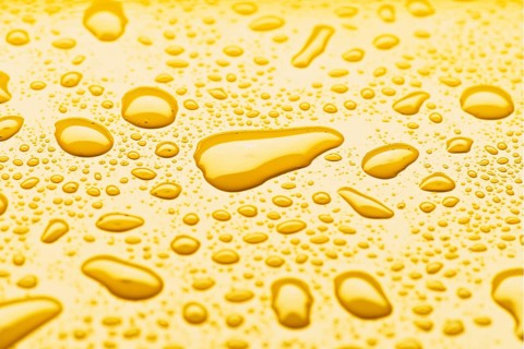 A close up image of yellow glossy liquid droplets on a surface, capturing the vibrant color and