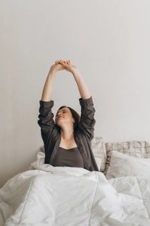A woman stretches in bed, embracing a fresh morning start. This routine promotes wellness and