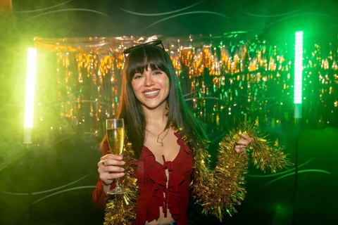 Young smiling woman celebrating during a party, holding a glass of champagne and gold tinsel