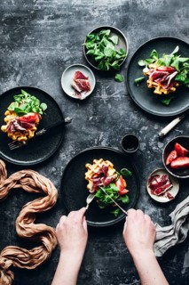 A combination of savory Iberian ham and pumpkin waffles served on dark plates. Garnished with fresh