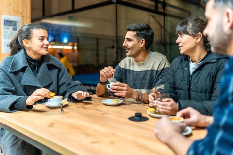 Group of diverse friends relaxing and having a conversation around a wooden table, drinking coffee