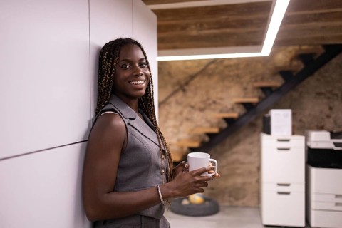 Young African woman with braids stands smiling holding a mug, enjoying a break in a contemporary