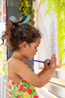 Young girl concentrating as she draws on a whiteboard at home. Her colorful dress and focused