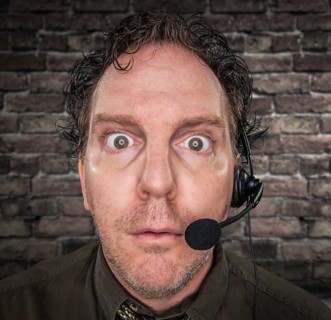Stunned Businessman Wearing Phone Headset In Office With Brick Wall Background
