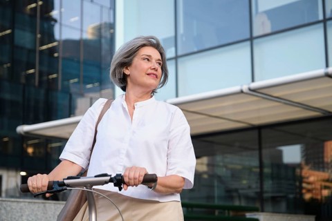 A mature woman with gray hair and a confident smile rides an electric scooter in an urban setting,