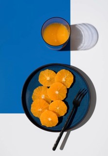 Overhead view of vibrant orange slices on a dark blue plate next to a glass of orange juice. The