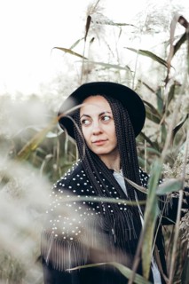A woman stands amidst tall grasses at sunset, her braided hair gently catching the last light of