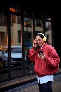 A man wearing yellow headphones, holding a smartphone, and smiling while enjoying music outside.