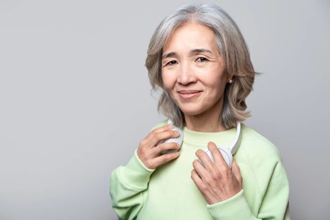 Asian Chinese senior woman in a light green sweater holding white headphones around her neck,
