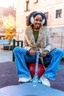 Young woman wearing earmuffs and winter clothes enjoys a playful moment on a playground rocker in a