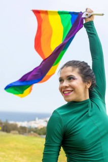 A joyful woman dances with a rainbow flag, embodying LGBTQIA+ pride in a vibrant outdoor setting.