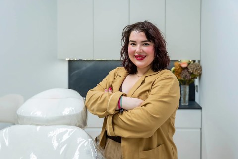 Confident female doctor smiling, standing in an aesthetic clinic room with a treatment chair,