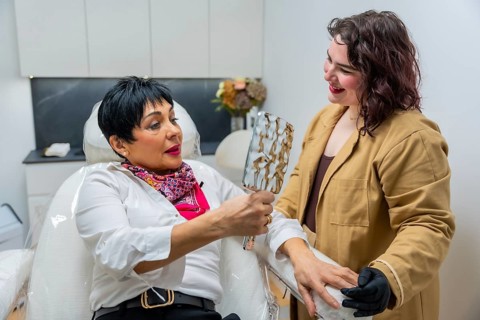 Patient sitting in a chair holding a mirror, discussing beauty and skincare treatments with a