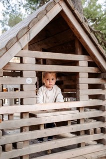 A young girl enjoys an afternoon in a wooden playhouse within a forest park. Surrounded by nature,
