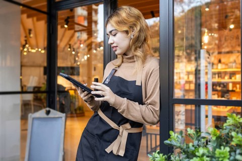 A worker in a cosmetics store stands at the entrance, using a tablet. The scene depicts a modern