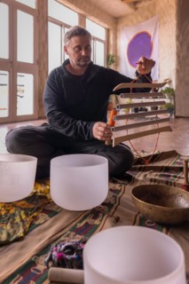 A mature Caucasian man playing a Samafon, a vibroacoustic instrument, surrounded by a collection of
