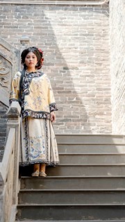 A woman in traditional Qing dynasty clothing stands on stone steps in Pingyao, China, looking at