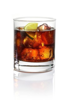 Whisky and cola on ice cube cubes in a tumbler against a white background, half a slice of lime as