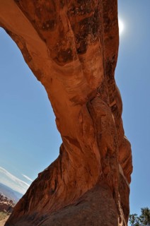 An impressive natural sandstone bridge with blue sky and sun in the background, Arches National