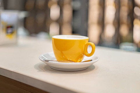 A vibrant yellow coffee cup sits gracefully on a white saucer at an airport cafe, inviting