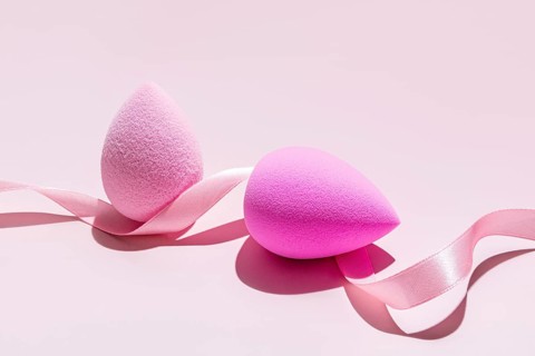 Makeup sponges, a pale and a vibrant pink beauty blender, elegantly intertwined with a silky pink