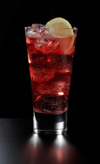 Cocktail Campari Soda in a long drink glass in front of a black background, half a slice of lemon
