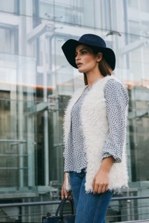 A fashionable woman in a chic fur vest and patterned top, accessorized with a modern black hat and