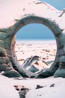 A striking circular ice arch frames a distant snowy horizon at Katla Glacier. The natural formation