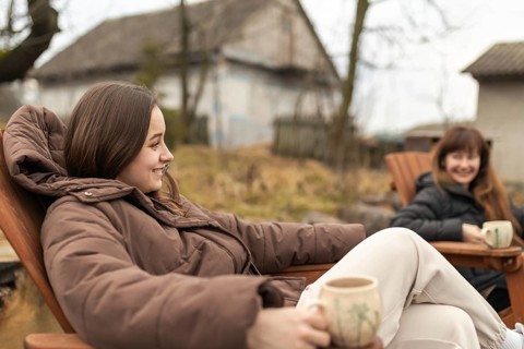 Female friends enjoy a cozy outdoor gathering, sharing laughs and warm drinks while seated in a