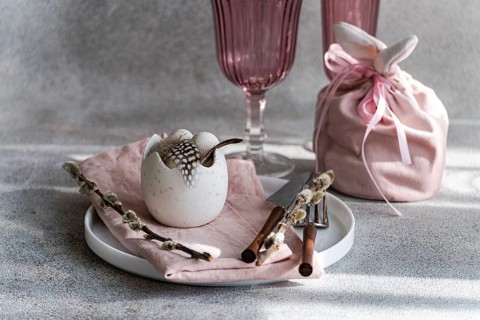 Beautifully arranged Easter table setting featuring a cracked eggshell vase with feathers,