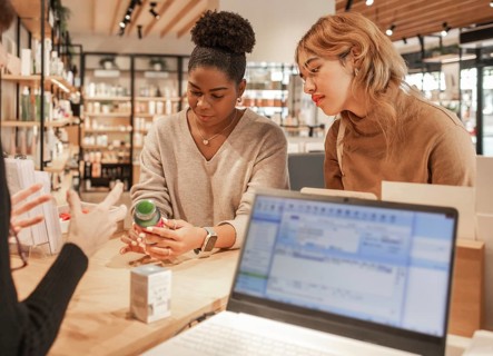 Two women attentively examine a product while receiving expert advice in a modern cosmetics store.