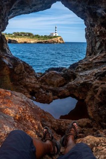 Tourist resting in arc natural cave framing portocolom lighthouse on mallorca island, enjoying
