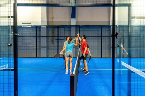Four friends share a celebratory high five on a blue indoor pickleball court, smiling after an
