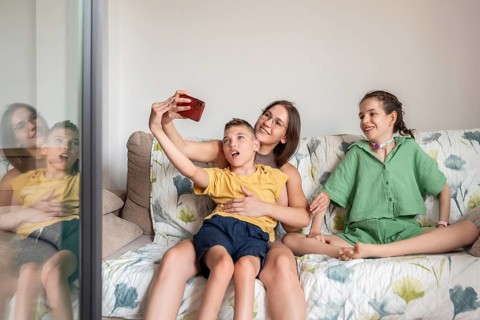 A joyful family shares a loving moment on the couch, capturing a selfie. The family includes a girl