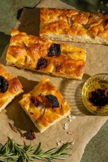 Slices of homemade focaccia topped with rosemary, roasted garlic, and sun dried tomatoes. Served on