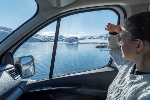 A woman gazes through a car window at the serene, snowy landscape of Botnhamn, Norway, with a calm